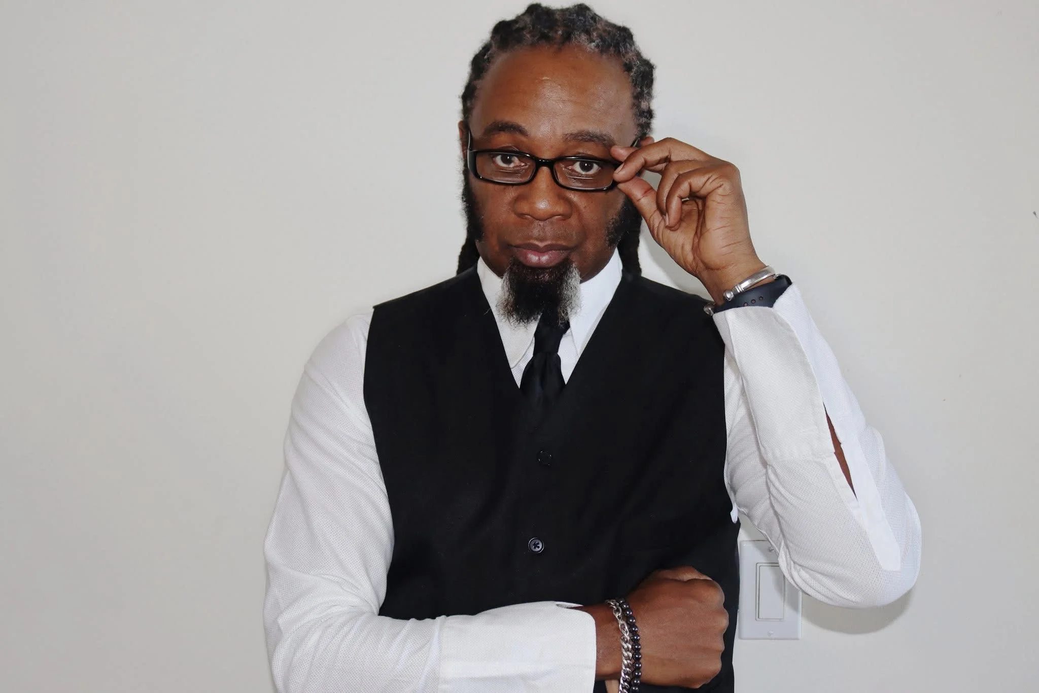 Victor E Lewis wearing a black vest, white shirt, and tie while adjusting his glasses